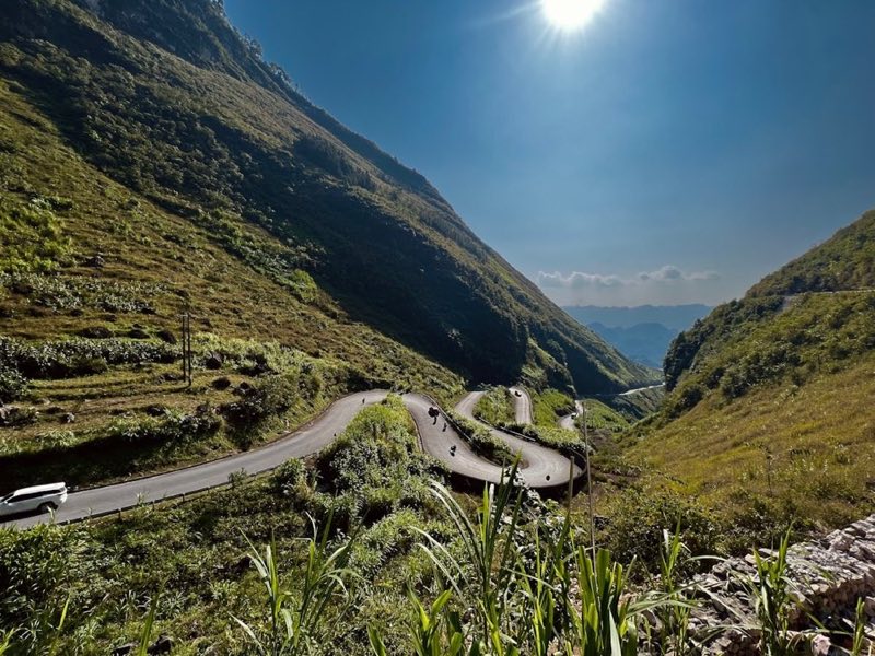 Winding mountain road through Ha Giang's limestone valleys with motorbikes on hairpin bends