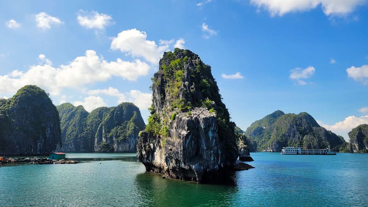 Limestone karst islands rising from Ha Long Bay's turquoise waters with a cruise junk visible