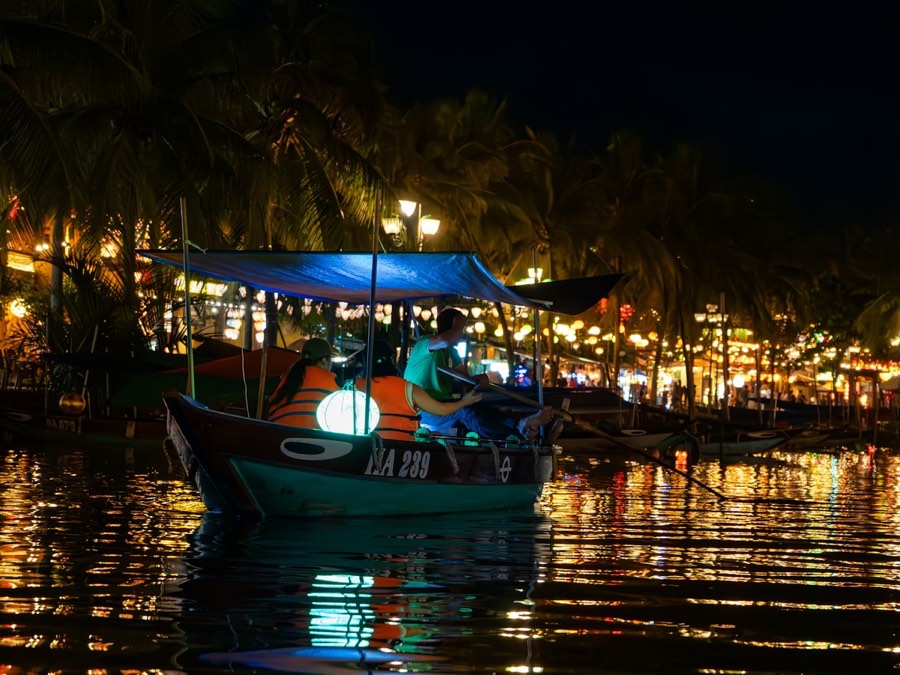 Illuminated paper lanterns reflecting on the Thu Bon River from a traditional wooden boat at night in Hoi An, Vietnam