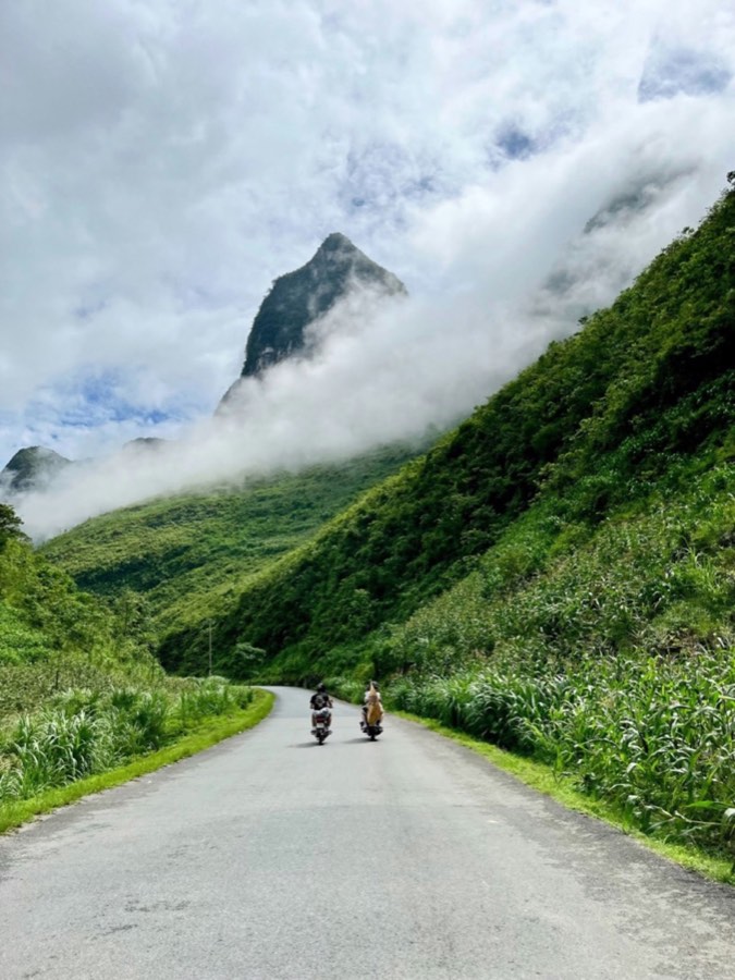 Two motorcyclists on a winding road through green mountains in Ha Giang, Vietnam