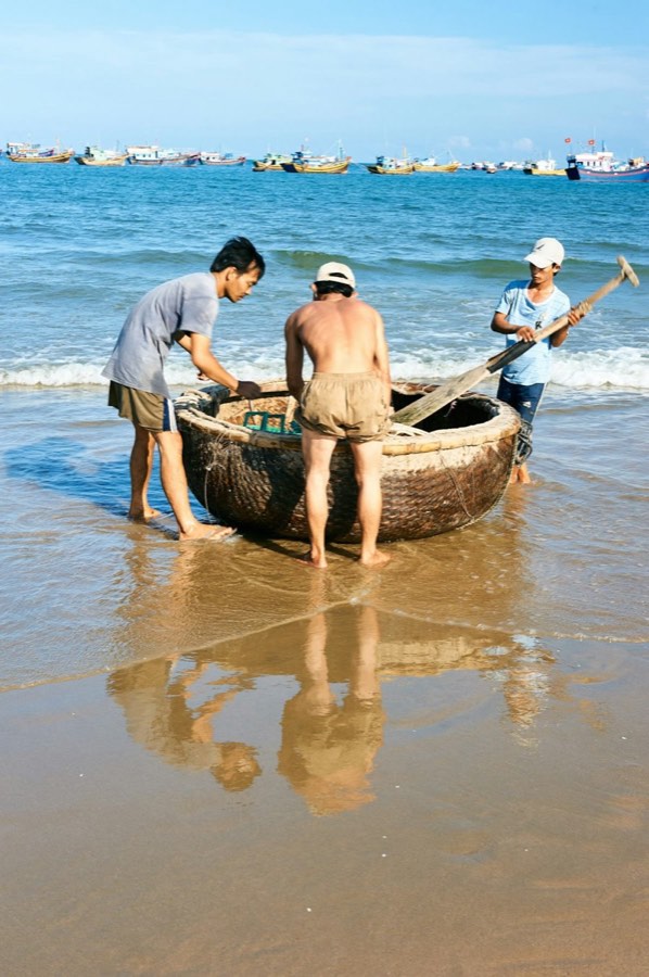 Fishermen launching a round boat on the beach, central Vietnam