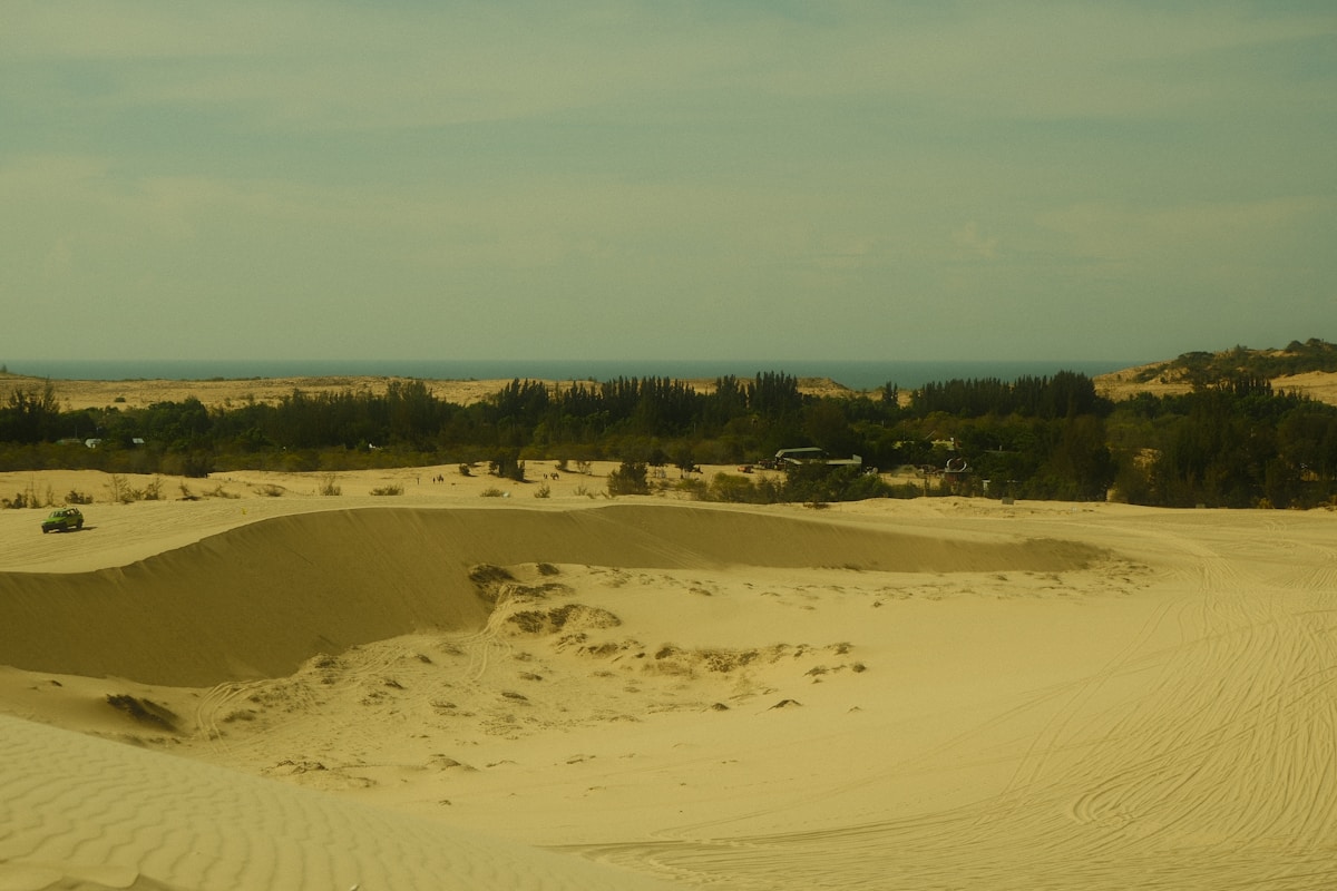 White sand dunes with a green jeep and trees meeting the ocean at Mui Ne, Vietnam