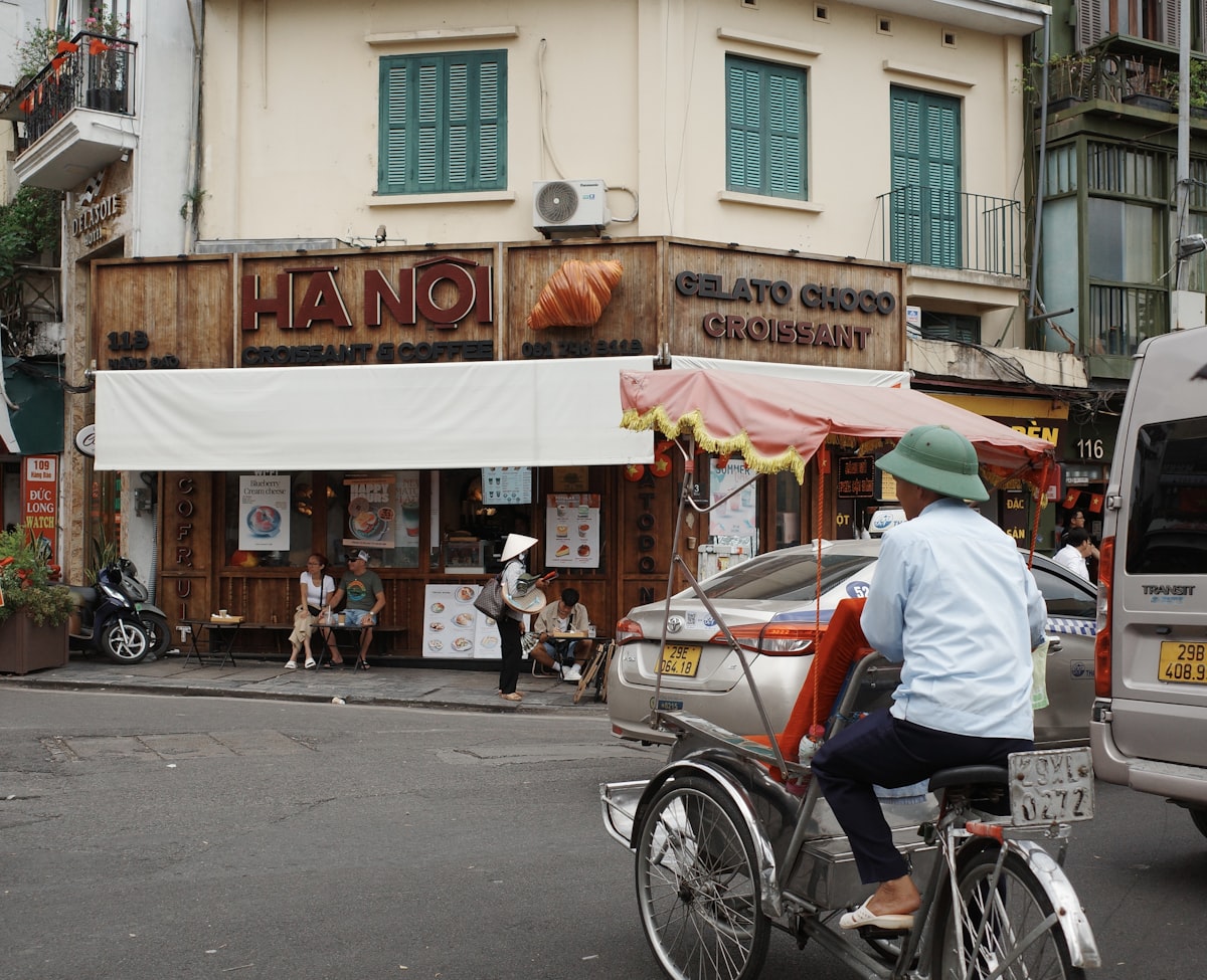 Street scene in Hanoi with a cyclo driver passing a café, Vietnam