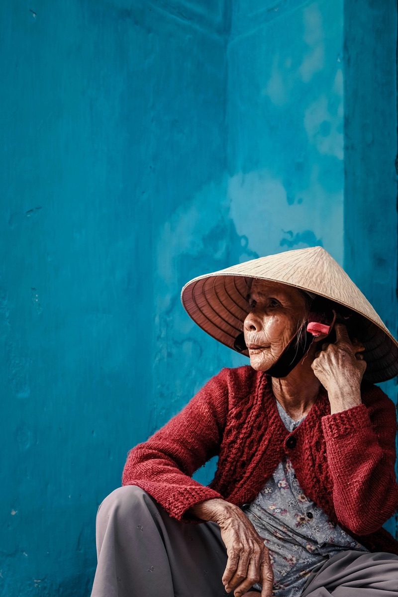 Vietnamese woman in conical hat sitting against turquoise wall in Hoi An