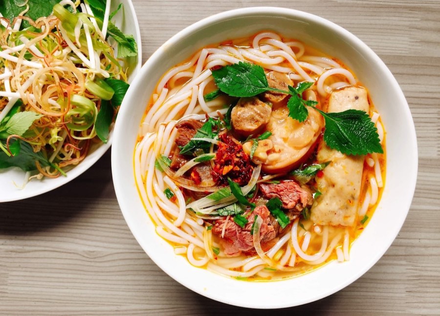 Bowl of Vietnamese pho noodle soup with beef, herbs and chopsticks