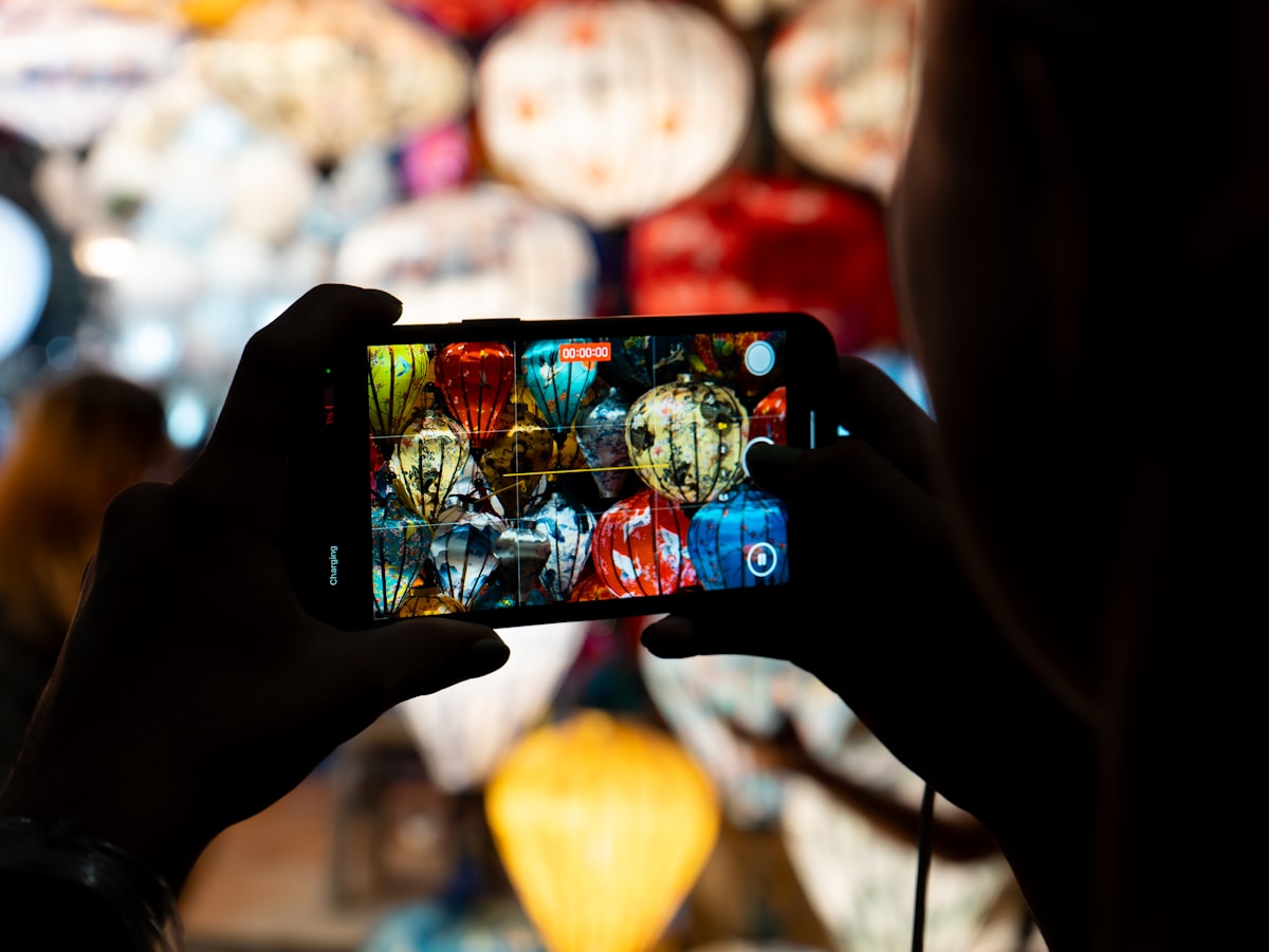 Person photographing Hoi An lanterns with smartphone, Vietnam