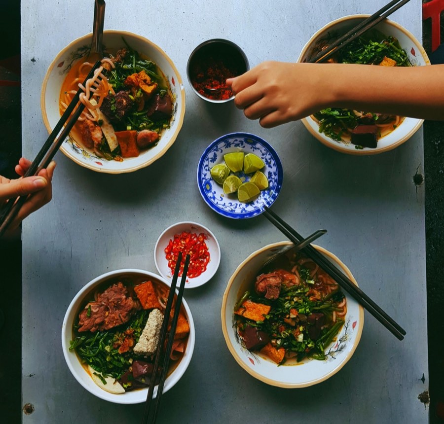 Bowls of Vietnamese noodle soup with chopsticks and fresh vegetables on a street-food table