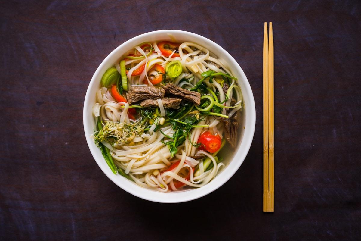 Bowl of Vietnamese beef noodle soup with fresh herbs, chilli and chopsticks
